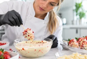 Chef de cozinha preparando morango cravejado com cobertura de chocolate branco e pedaços de morango